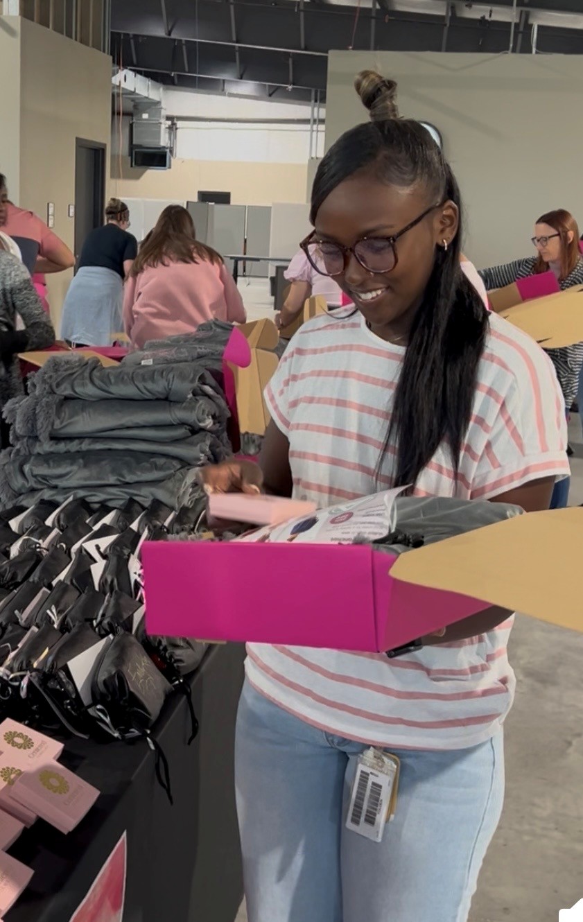 a volunteer helps pack a pink breastie box with supplies